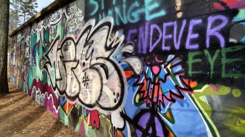 An old wall is covered with graffiti. Portions of words can be seen, some abstract; a cat's face; the sentence "let's keep this a place for art."