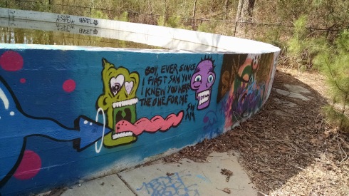 An old water holding tank is covered with graffiti. An image painted on blue background shows two monster heads, one with a long tongue sticking out towards the other, and the caption, "Boy, ever since I first saw you I knew you were the one for me."